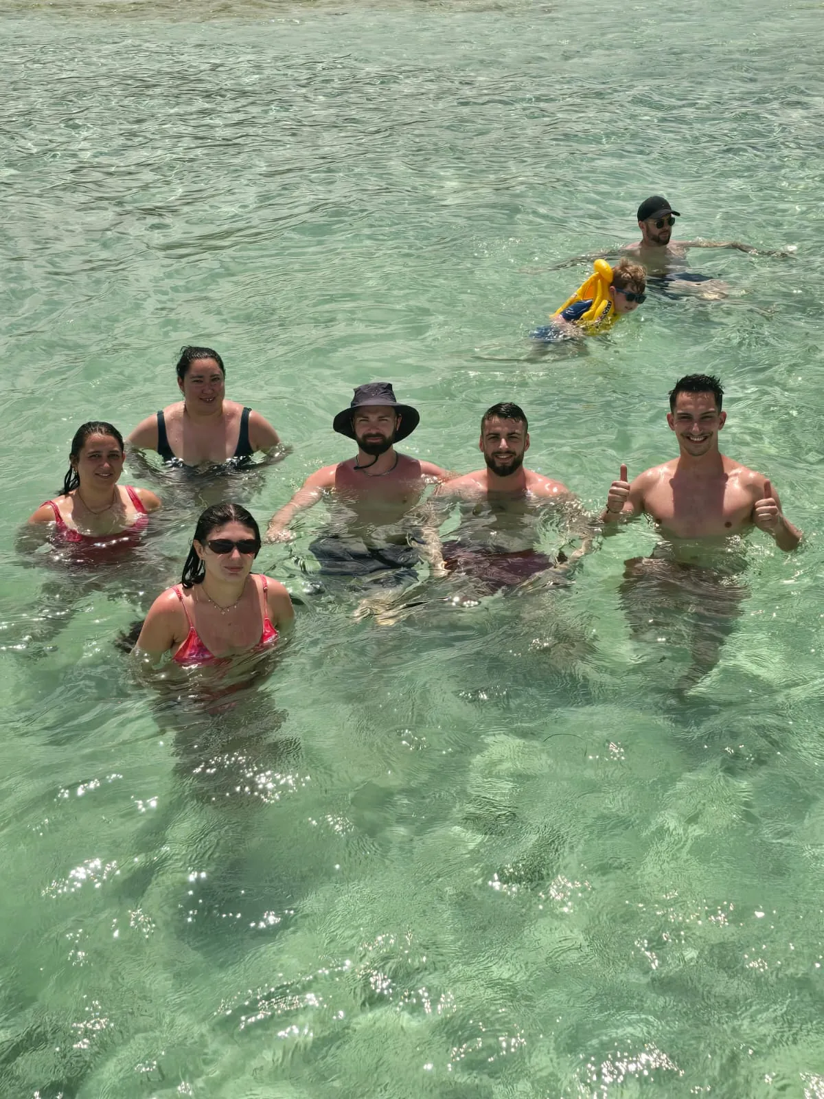 Groupe de vacanciers debout dans l'eau claire et peu profonde des fonds blancs, Martinique