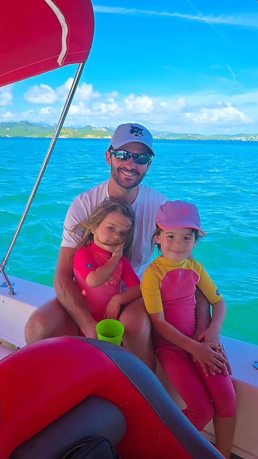 Un père et ses deux filles assis à bord d'un bateau devant les eaux turquoise des fonds blancs