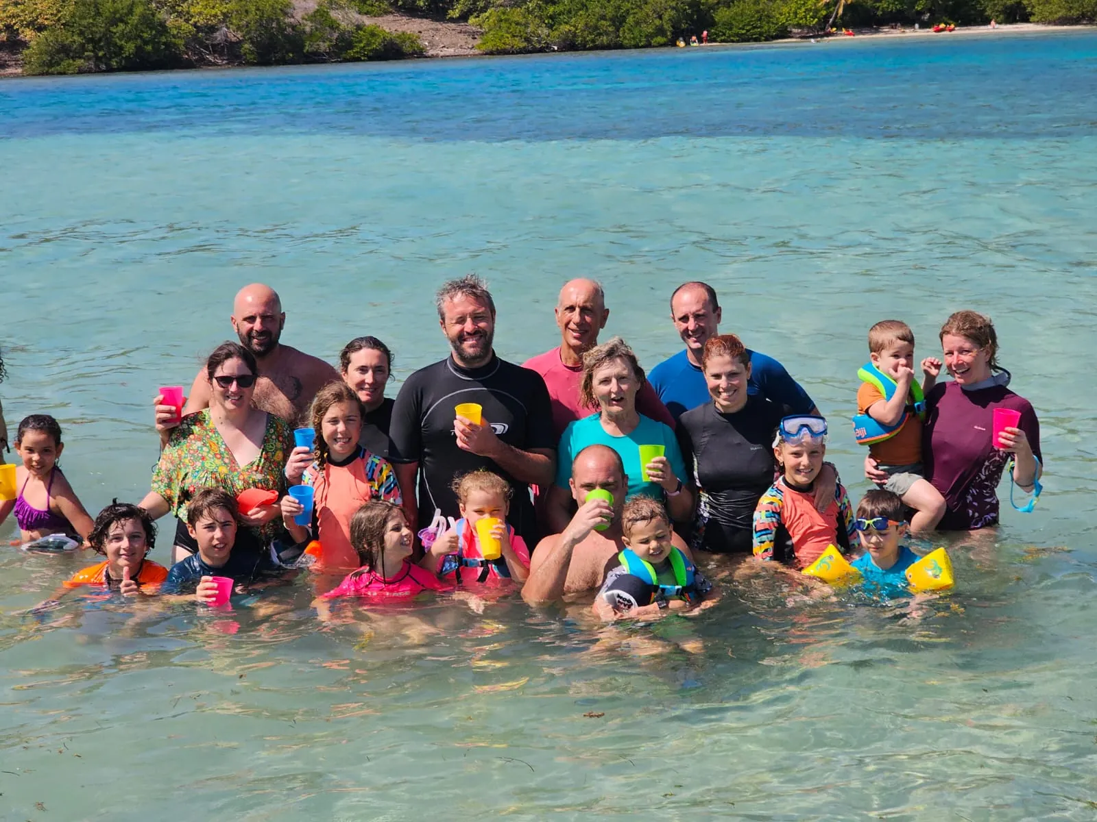 Groupe de vacanciers de tous âges trinquant, debout dans l'eau peu profonde des fonds blancs