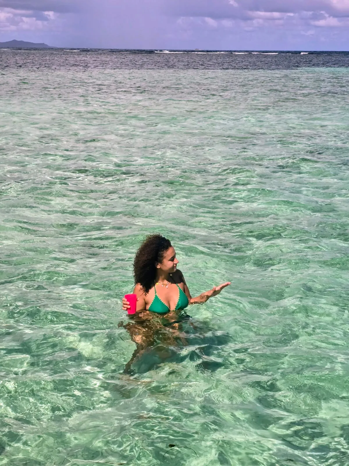Une baigneuse tient son gobelet dans l'eau turquoise et peu profonde des fonds blancs