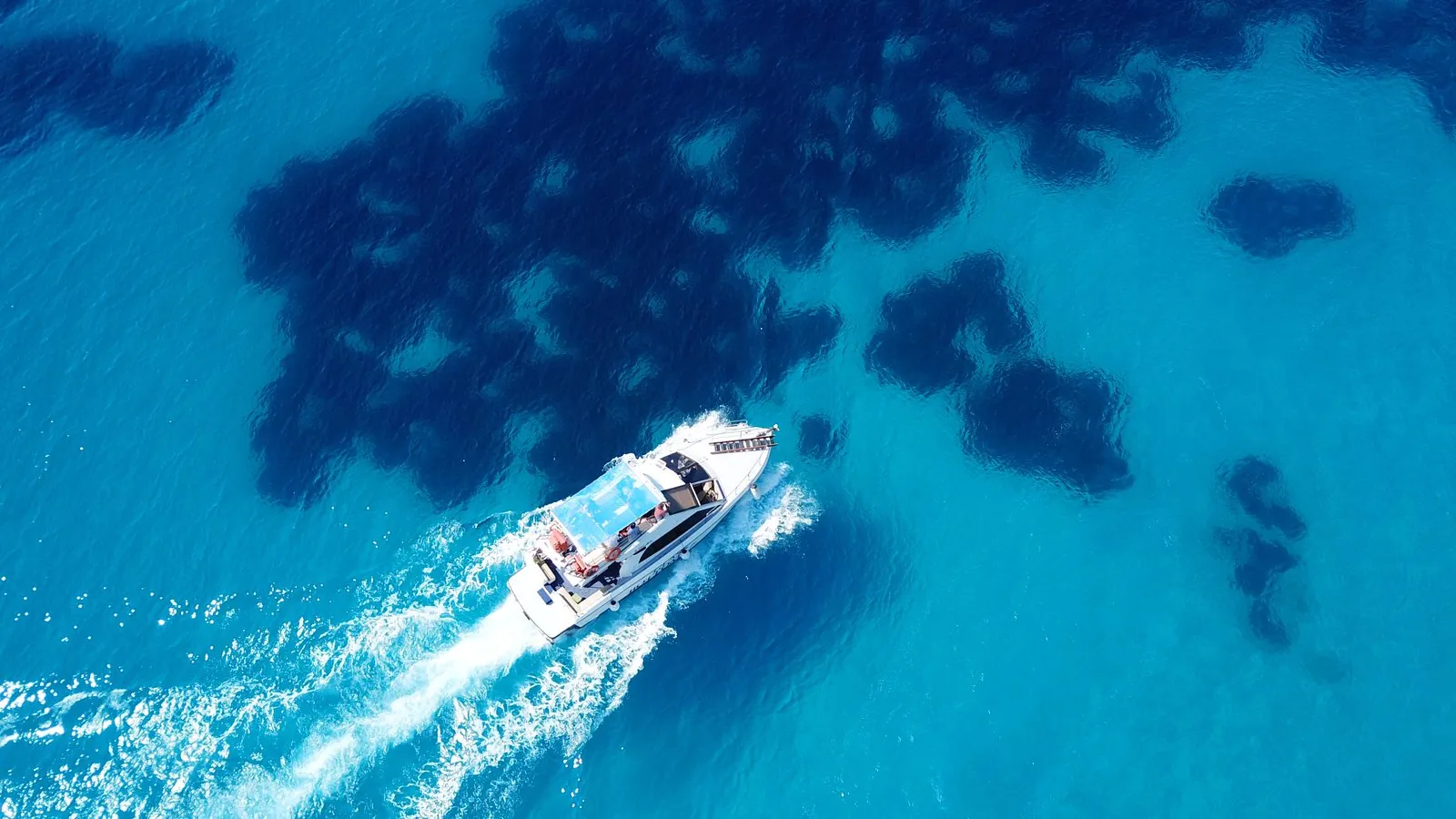 Vue zénithale d'un bateau d'excursion et de ses passagers filant sur des fonds turquoise