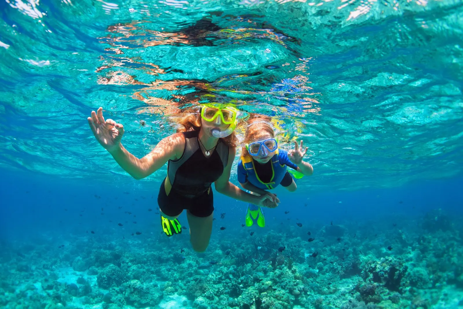 Une mère et son enfant masqués et palmés nagent au-dessus d'un récif corallien dans une eau turquoise